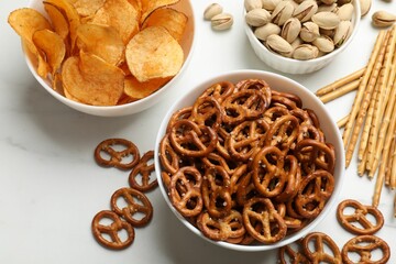 Delicious pretzel crackers and other snacks on white table, flat lay