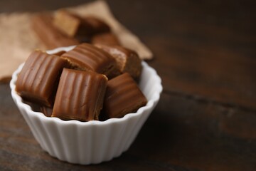 Tasty sweet caramel candies in bowl on wooden table, closeup