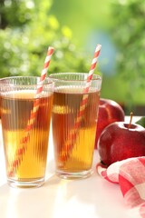 Tasty apple juice in glasses and fresh fruits on white table outdoors