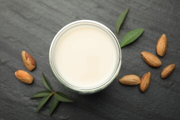 Fresh almond milk in glass, nuts and leaves on black table, top view