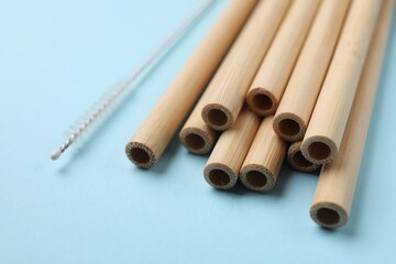 Bamboo drinking straws and cleaning brush on light blue background, closeup