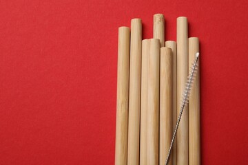 Bamboo drinking straws and cleaning brush on red background, top view. Space for text