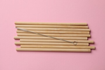 Bamboo drinking straws and cleaning brush on pink background, top view