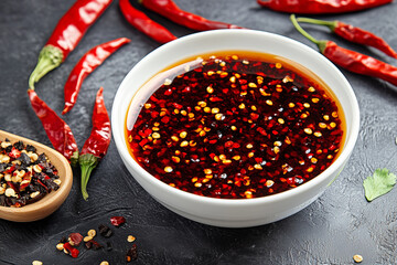 A bowl of spicy chili oil filled with red pepper flakes, surrounded by whole red chilies and a small wooden spoon with mixed spices.