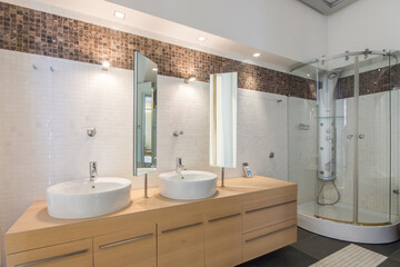 Bathroom with modern shower cabin. Beige cabinet with sink bowls and rotating mirrors.