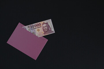 A Hungarian banknote is visible in the envelope. It is in a purple envelope on a black background.