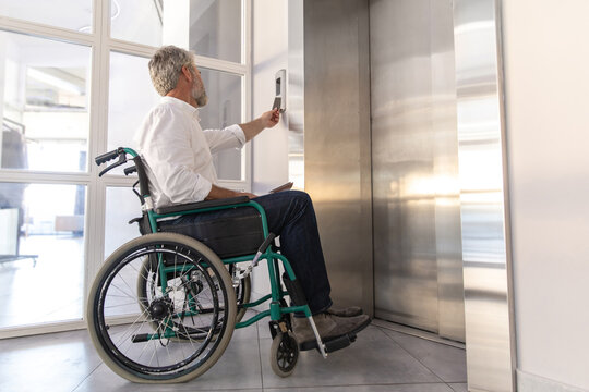 Male entrepreneur with disabilities in wheel chair waiting for elevator in office