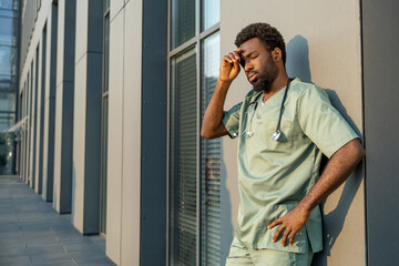 Male nurse standing outdoors wearing medical uniform and stethoscope near the hospital
