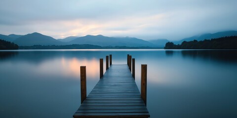 Naklejka premium Serene Lake Pier Leading to Misty Mountains at Dawn