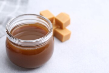Tasty caramel sauce in jar and candies on light table, closeup. Space for text