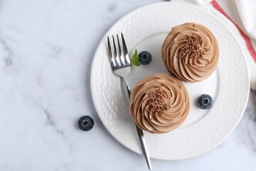 Tasty cupcakes with chocolate cream and blueberries on white marble table, top view. Space for text