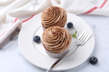 Tasty cupcakes with chocolate cream and blueberries on white marble table