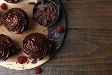 Tasty cupcakes with chocolate cream and raspberries on wooden table, flat lay. Space for text
