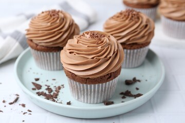 Tasty cupcakes with chocolate cream on white tiled table, closeup