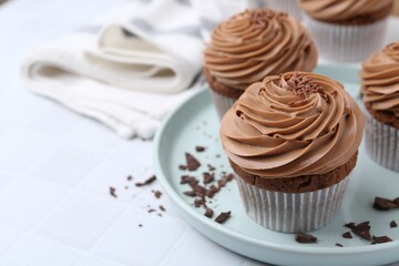 Tasty cupcakes with chocolate cream on white tiled table, closeup. Space for text