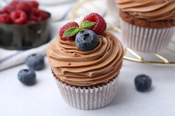 Tasty cupcakes with chocolate cream and berries on white table, closeup