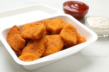Tasty chicken nuggets and sauces on white marble table, closeup
