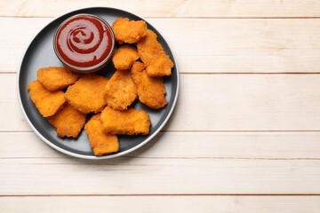 Tasty chicken nuggets and sauce on wooden table, top view. Space for text