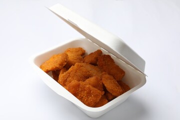 Delicious chicken nuggets in takeaway container on white background