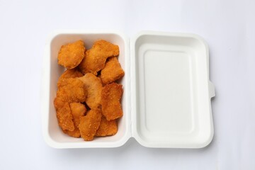 Delicious chicken nuggets in takeaway container on white background, top view