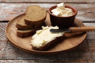 Fresh bread with butter and knife on wooden table, closeup