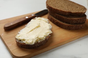 Fresh bread with butter and knife on white table, closeup