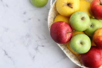 Different ripe apples in basket on white table, flat lay. Space for text