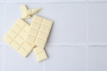 Pieces of delicious white chocolate on tiled table, top view. Space for text
