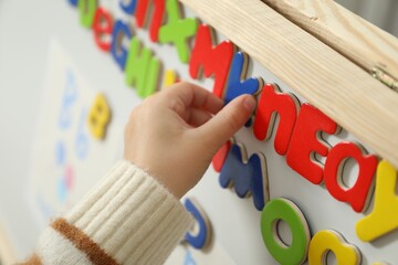 Little girl learning alphabet with magnetic letters indoors, closeup