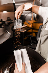 Packing roasted coffee beans into a craft bag. Pouring fried coffee grains in packaging bag in the facility.