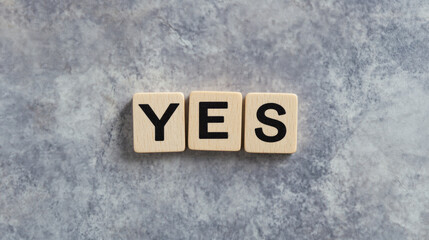 Wooden tiles spell out the word "YES" against a gray marbled background. Useful for concepts related to positivity, agreement, affirmation, and motivation.