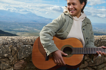 Woman smiling while playing guitar against scenic mountain view