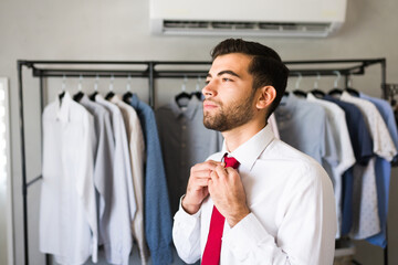 Businessman is adjusting his red tie in his walk in closet full of shirts getting ready for work