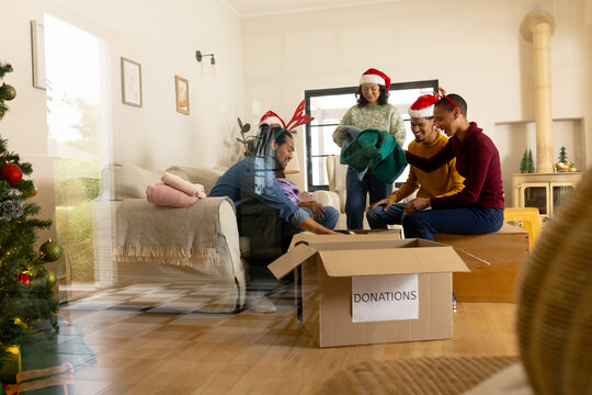 Young multiracial friends packing donations in living room during christmas, at home