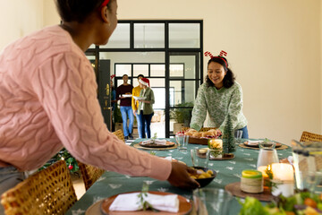 Preparing festive dinner table, multiracial friends wearing christmas accessories,at home