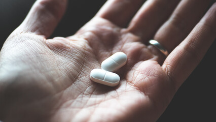 A hand holding white pill medicine minimalist close up