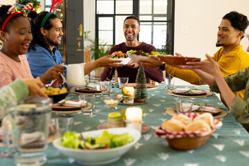 Christmas time, multiracial friends sharing festive meal at home, smiling