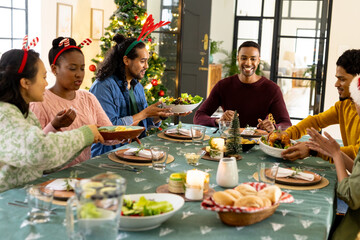 Obraz premium Young multiracial friends enjoying festive christmas dinner together, at home