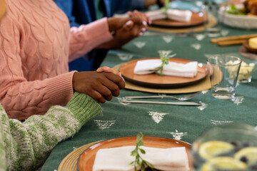 Christmas time, multiracial friends holding hands at festive dinner table, at home