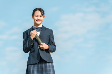 青空の下で卒業証書の丸筒を持つ卒業生の女子中学生
