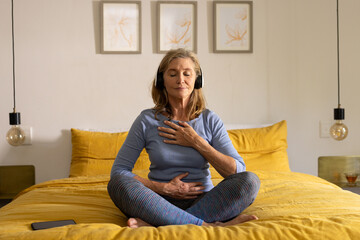 senior woman meditating on bed with headphones, enjoying peaceful moment, at home