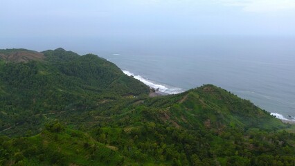 Drone view of Jerit hill Kebumen Indonesia, the seaside with beautiful hills and green trees, coral rocks, waves and ocean