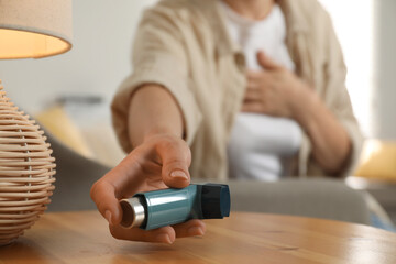 Woman holding asthma inhaler at wooden table indoors, closeup