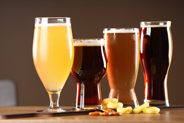 Glasses with different types of beer and snacks on wooden table indoors, closeup