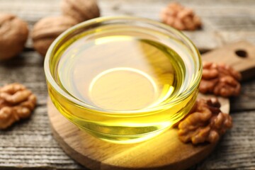 Cooking oil in bowl and walnuts on wooden table, closeup