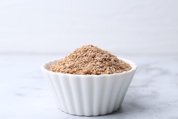 Buckwheat bran in bowl on white marble table, closeup