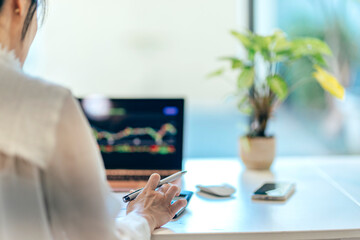 A mother in her home office reviews annual expenses and taxes, with a stock chart displayed on her computer screen, balancing family budgeting and investments.