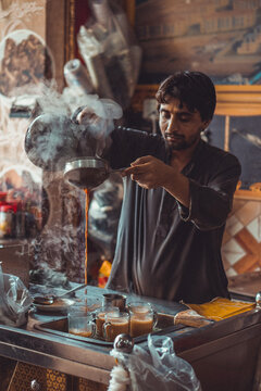Pakistani street vendor pouring chai tea into cups in his roadside tea stall