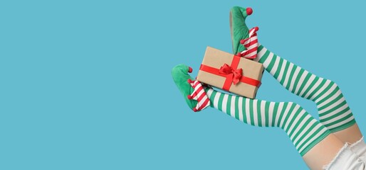 Legs of young woman in elf shoes, striped stockings and with gift on blue background with space for...