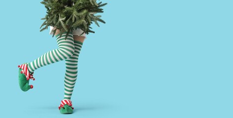 Legs of young woman in elf shoes and with fir tree branches on blue background with space for text